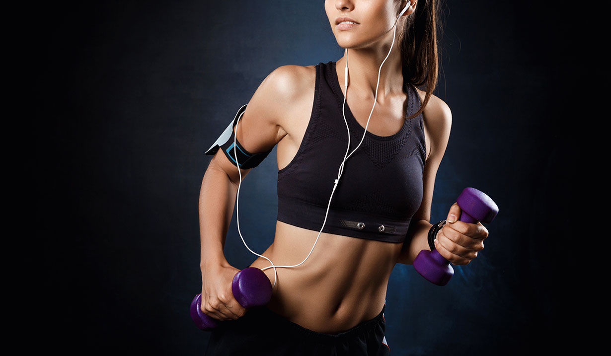 Young beautiful sportive girl training with dumbbells over dark background.